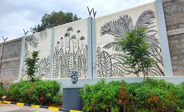 Road 23 inside the Sattva Green Groves layout, with a planted edge and a mural wall, site photo, September 2026